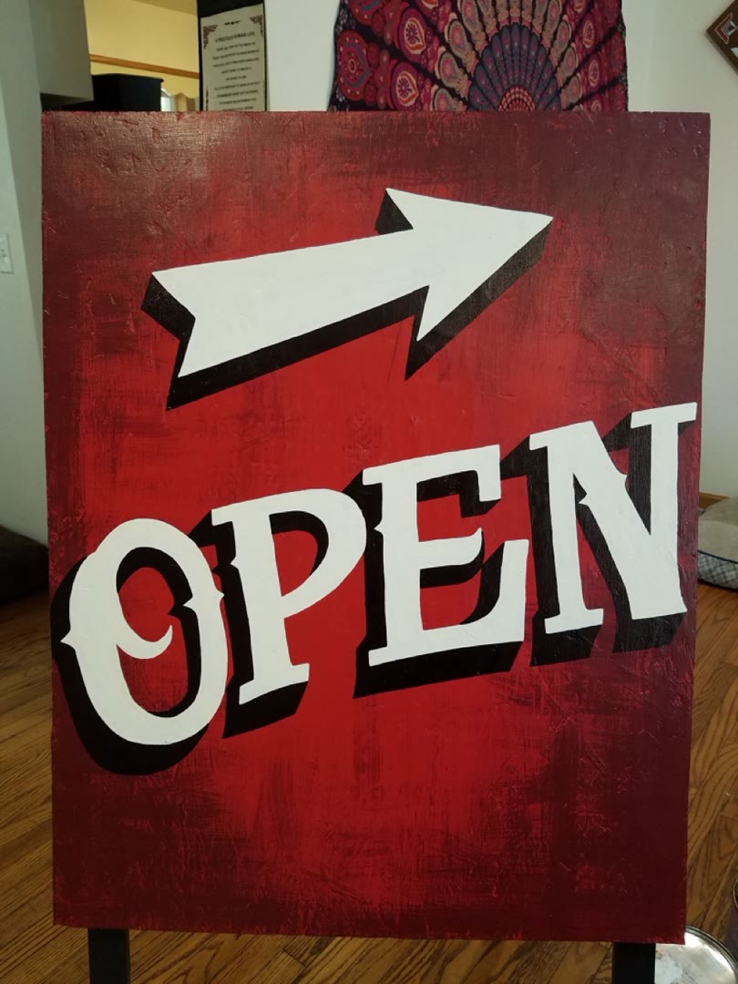 Hand-painted red open sign with a white dimensional arrow