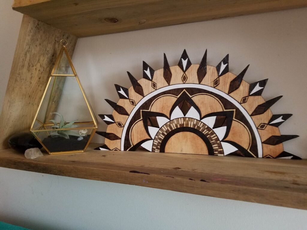 Hand-burned semicircular sunburst wood piece displayed on a shelf