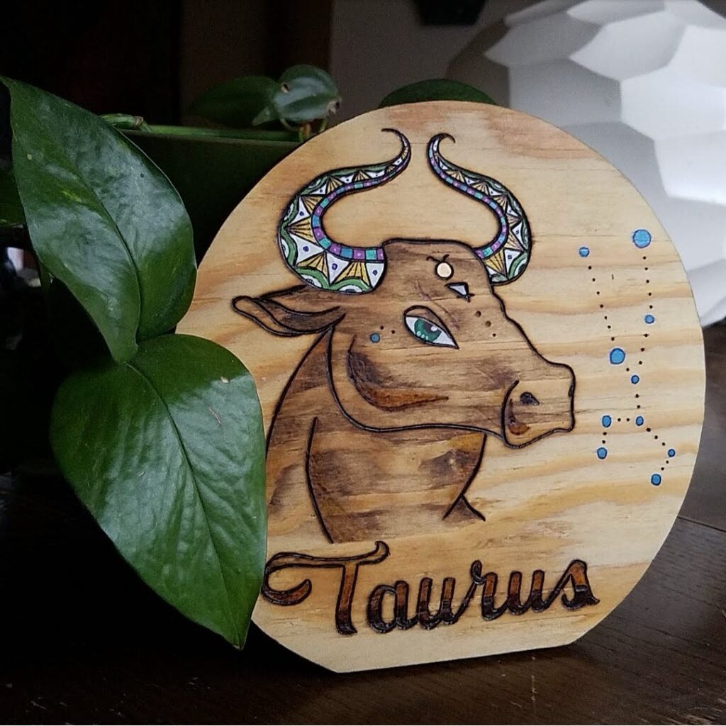 Round wood sign with a hand-burned Taurus bull illustration and decorative horns