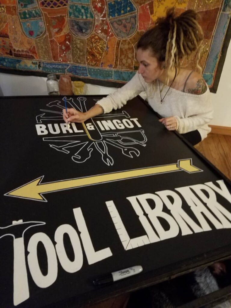 Detail of Journey Hallows painting the Burl and Ingot Tool Library sign